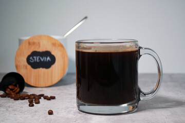 A glass of black coffee and a bowl with stevia sweetener, grey background 