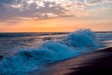 Waves on the shore of black sand beach of volcanic origin on the coast of Guatemala, sunset.