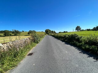 View along, Slaidburn Road, with dry stone walls, wild plants, fields, and a blue sky in, Grindleton, UK