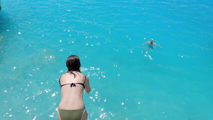 Young couple enjoy summer vacation jumping from high rock on Kathisma beach in Lefkada tuquoise water, slow motion