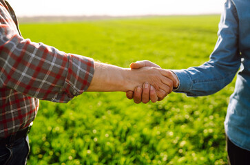 Two farm owners shake hands on a green field. Successful deal. Agriculture and business concept.