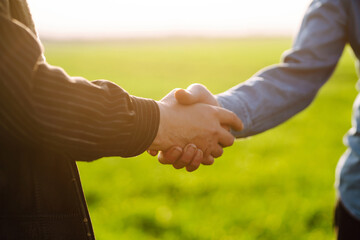 Two farm owners shake hands on a green field. Successful deal. Agriculture and business concept.