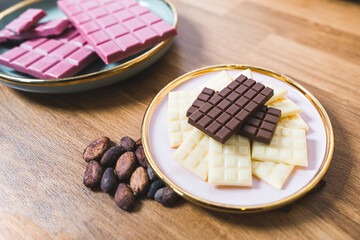 Plates with handmade chocolate bars. Premium candy concept. Ruby dark and white chocolate and chocolate beans laid out on wooden table. High quality photo