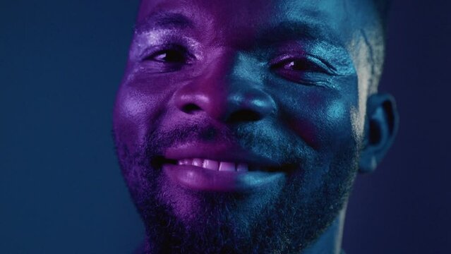 Close up portrait of a beautiful African American man in the studio. Attractive millennial guy opens his eyes, neon blue pink light. Professional male model. Art make up, beauty fashion