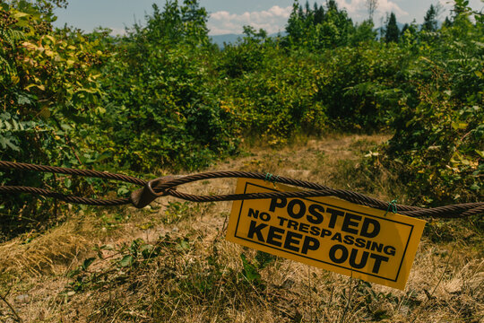 yellow sign stating "posted no trespassing keep out" on metal cord in forest, woods, land, private property, forbidden forest