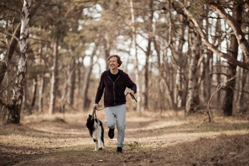 Mature man jogging in the forest with his border collie dog