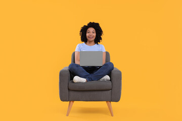 Fototapeta na wymiar Happy young woman with laptop sitting in armchair against yellow background