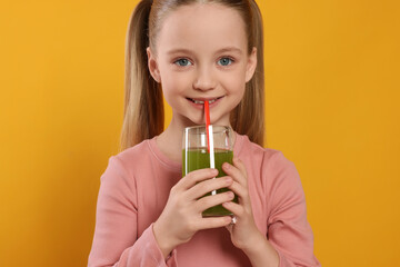 Fototapeta premium Cute little girl drinking fresh juice on orange background