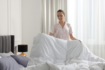 Young beautiful woman making bed in room