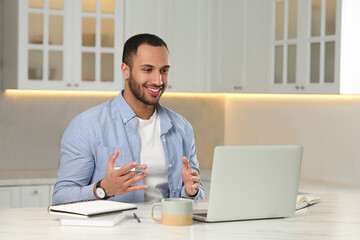 Fototapeta premium Young man having online video chat at desk in kitchen. Home office