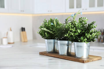 Different artificial potted herbs on white marble table in kitchen, space for text