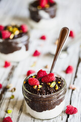 Dark chocolate chia pudding with raspberries and pistachios on top in a glass jar on a white wooden background. Served with coconut whipped cream. Healthy food. Copy space.
