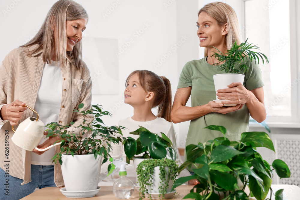 Wall mural Three generations. Happy grandmother, her daughter and granddaughter watering houseplants at home