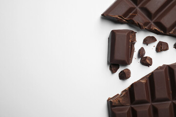 Pieces of delicious dark chocolate bar on white background, flat lay. Space for text