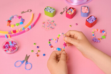 Child making beaded jewelry and different supplies on pink background, above view. Handmade accessories