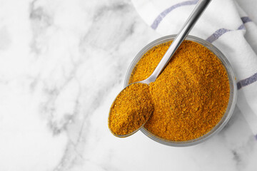 Glass with curry powder and spoon on white marble table, top view. Space for text