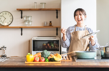 キッチンで料理の味見をするエプロン姿の女性・主婦（カフェ）
