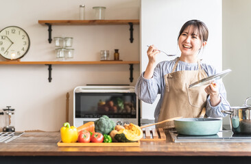 キッチンで料理の味見をするエプロン姿の女性・主婦（カフェ）

