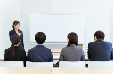 オフィス・会議室で研修・セミナーを受けるスーツを着た男女の後ろ姿
