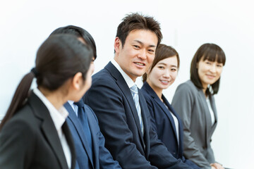 会社・オフィスで椅子に座るスーツ姿の会社員・従業員・スタッフ・同僚（アジア人・男女・5人）
