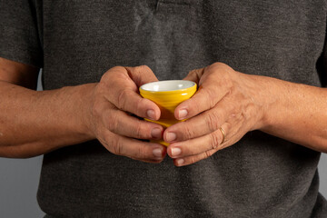 Hands of an elderly man holding a mug with a hot drink