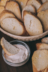 Pieces of roasted white bread in wicker basket and glass bowl of sauce on a dark background. Closeup of delicious croutons.