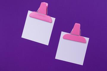 White paper notes with pink paper clip holders isolated on purple background. Blank notes on purple.