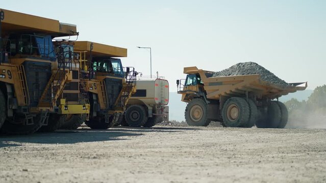Big dumper trucks on a construction site transporting ore from open mine pit, slow motion