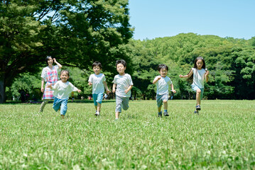 緑地でかけっこをする子供たちと、見守る女性