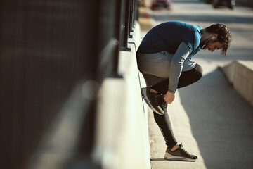 Young adult man tying his shoelaces while jogging in the city