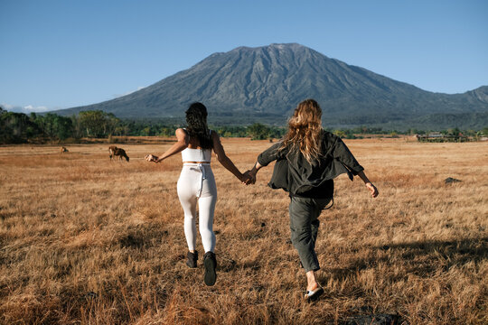 A pair of young people in love, a man and a girl, of European appearance with long hair, hold hands and run across a field of dry, yellow grass, against the backdrop of a huge mountain.