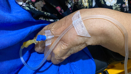 Close up hand of senior patient with intravenous catheter for injection plug in hand during lying in the hospital bed.