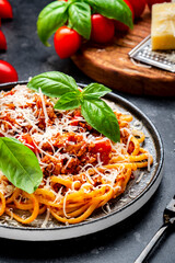 Spaghetti bolognese or pasta with minced meat in tomato sauce with green basil sprinkled with grated parmesan cheese, dark table, top view