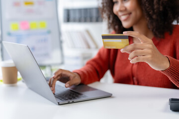 Woman using laptop computer and credit card for online shopping at home. Female happily utilizes her laptop and credit card for convenient online purchases.