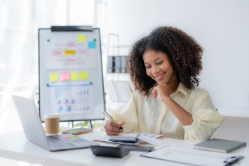 Happy young businesswoman sitting at desk and take notes with laptop computer in the office.