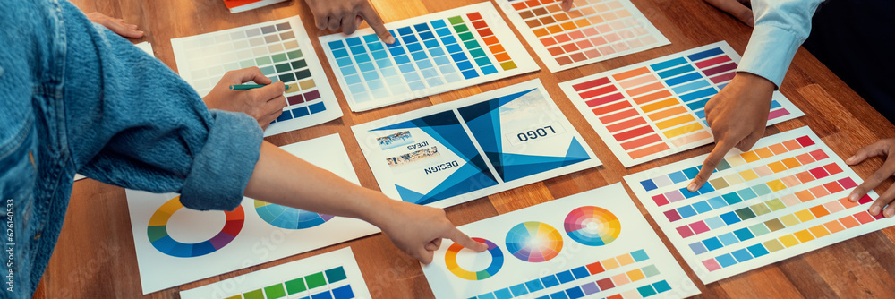 Poster Graphic designer brainstorm logo and graphic art at busy creative studio workshop. Experiment and brainstorm color palette and pattern at workspace table for creative design. Panorama shot. Scrutinize