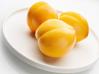 Three yellow nectarines on a white plate close-up. Light background. White background. Studio shot. Horizontal.