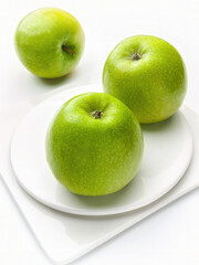 Three green apples, Granny Smith on white dishes, white background, selective focus, vertical shot, studio.