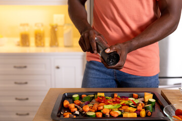 Midsection of african american man seasoning vegetables in kitchen