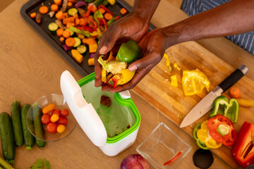 Hands of african american man composting vegetable waste in kitchen