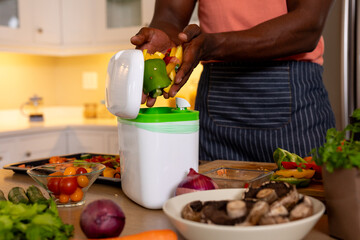 Midsection of african american man composting vegetable waste in kitchen