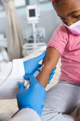 Obraz premium African american female doctor wearing face mask vaccinating girl patient at hospital