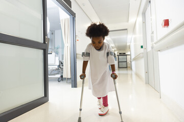 African american girl patient walking with crutches in corridor at hospital