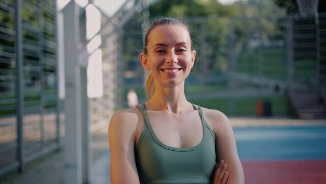 Pretty athletic girl in green sportswear puts her hands together on the sports field. Portrait of a confident beautiful woman in the morning outdoor, healthy female sportswoman looking at camera.