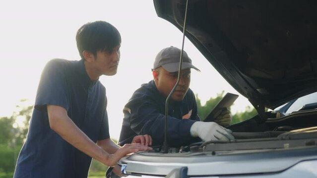 Handsome asian mechanic man shows the car report on a digital tablet to asian client at the roadside, A mechanic and a customer discussing repairs problems to his vehicle. 4k resolution.