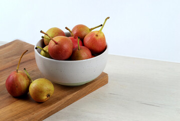 White bowl with small pears on wooden board