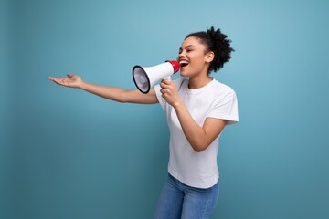 latin young woman dressed in a white t-shirt and talking a message into a megaphone on a blue...