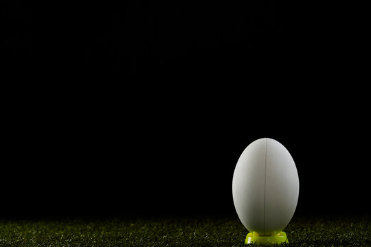 White rugby ball in yellow stand over grass with copy space, in slow motion