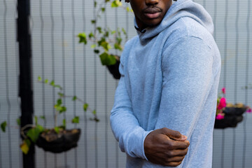 Midsection of african american man wearing grey hooded sweatshirt against white fence, copy space