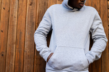 Midsection of african american man wearing grey hooded sweatshirt against wooden fence, copy space